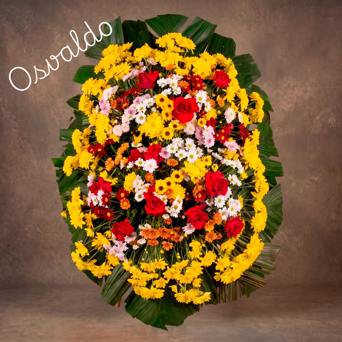 Coroa oval de crisântemos amarelos na borda, com rosas vermelhas, margaridas brancas e flores laranja no centro, sobre folhas de palmeira.